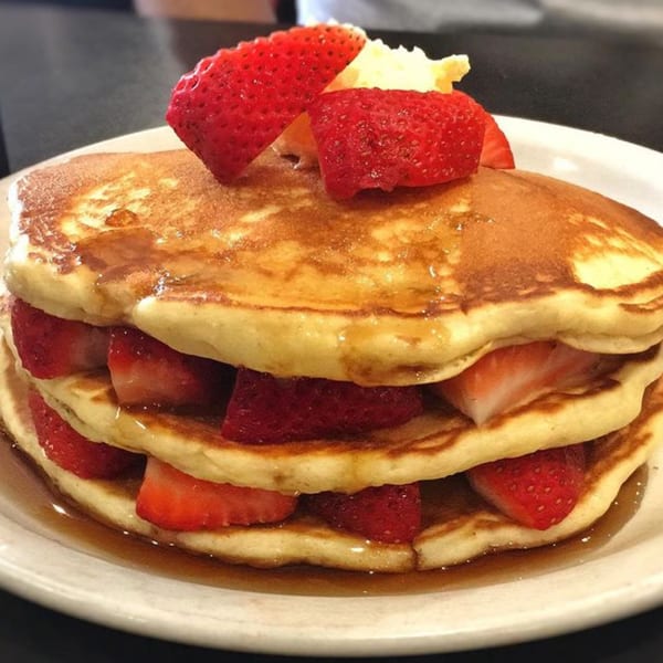 Stack of Good Day Cafe pancakes with strawberries, butter, and syrup on a white plate.