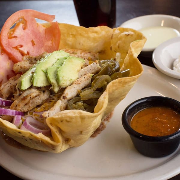 A taco salad in a crispy tortilla bowl with chicken, avocado, tomatoes, onions, and jalapeños.