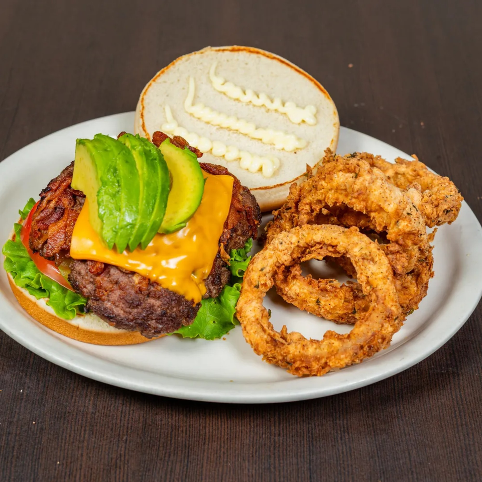 Good Day Cafe's avocado cheeseburger with bacon, lettuce, tomato, and a side of crispy onion rings.