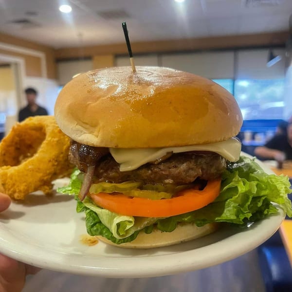 Good Day Cafe's cheeseburger with lettuce, tomato, pickles, and onion rings on a white plate.