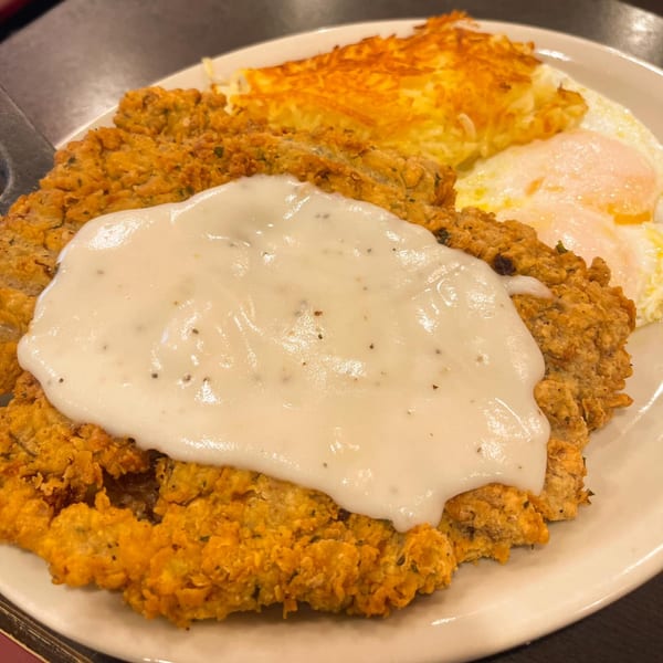 Chicken fried steak with gravy, hash browns, and two fried eggs on a white plate.