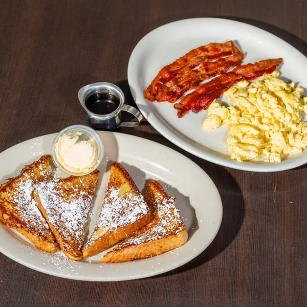 Good Day Cafe's French toast with powdered sugar, butter, syrup, bacon, and scrambled eggs.
